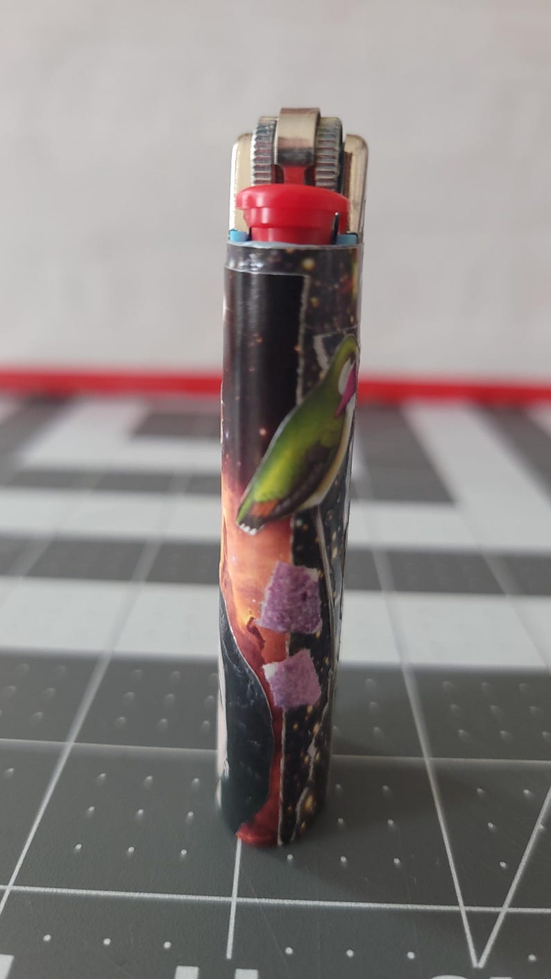 May include: A silver lighter with a red top and a colorful design featuring a bird and a galaxy-like background.