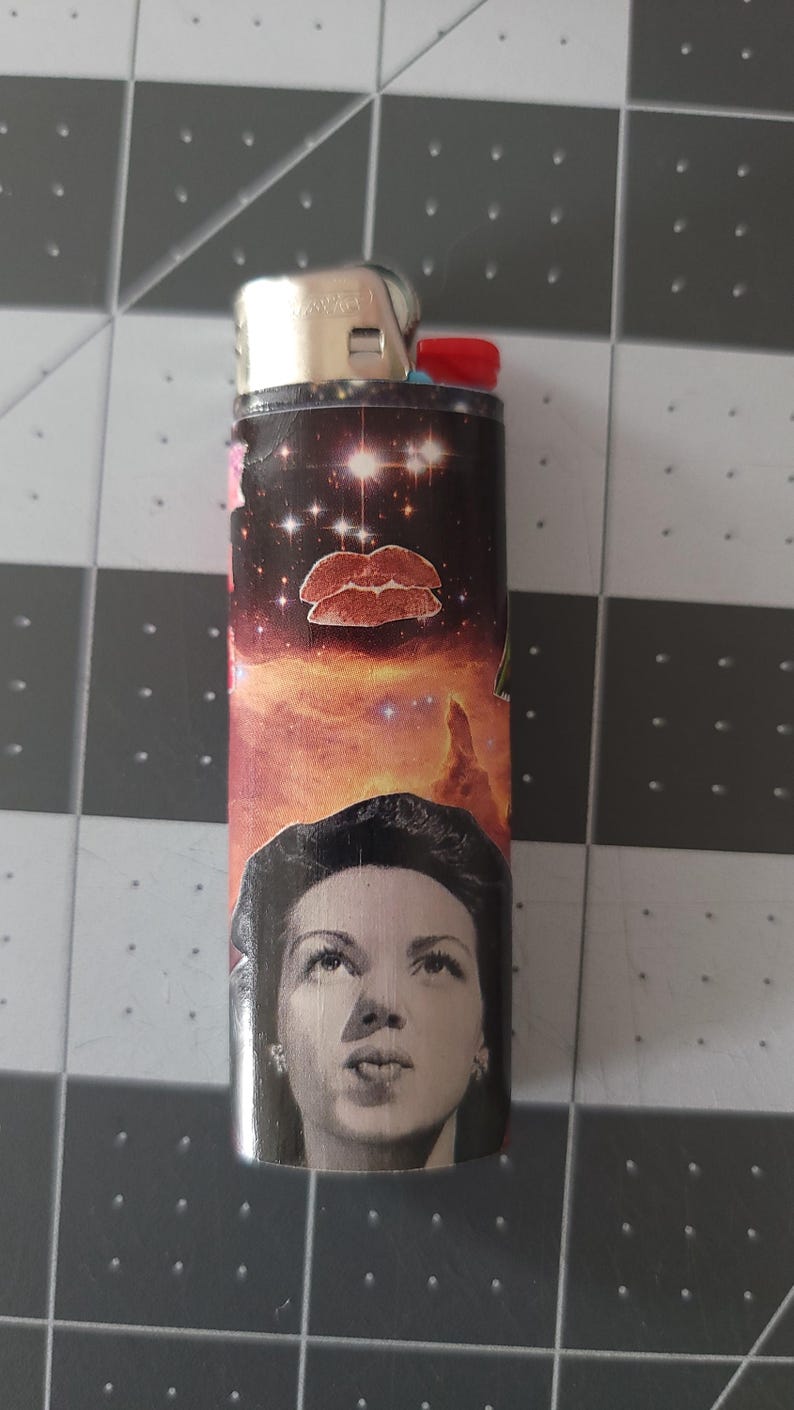 May include: A black lighter with a colorful design featuring a woman's face, a pair of lips, and a galaxy-like background.
