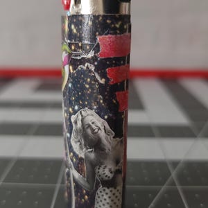 May include: A black and white lighter with a collage of images, including a woman in a polka dot bikini, a red and white stripe, and a starry sky.