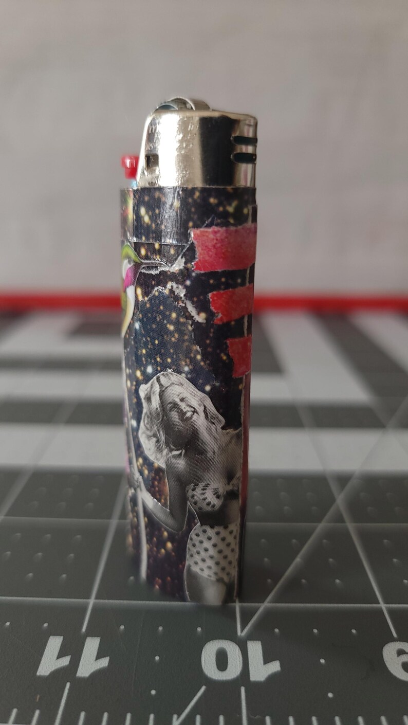 May include: A black and white lighter with a collage of images, including a woman in a polka dot bikini, a red and white stripe, and a starry sky.