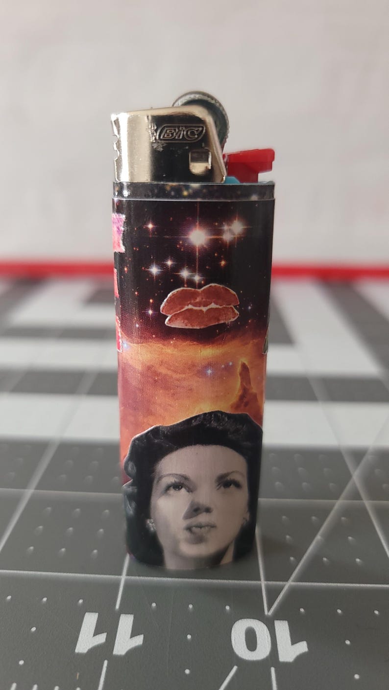 May include: A black and silver lighter with a colorful design featuring a woman's face, a galaxy, and red lips. The lighter has the word "BIC" printed on it.