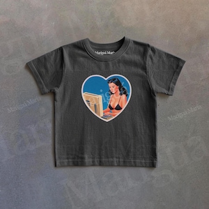 Puede incluir: Una taza de cerámica blanca con un asa negra y el texto "But First, Coffee" en negrita negra. La taza está llena de un líquido oscuro, probablemente café, y se encuentra sobre una superficie clara.