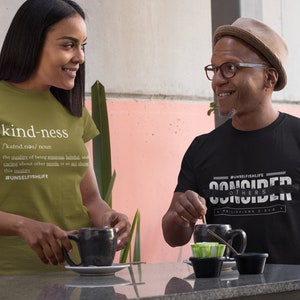 May include: Two people wearing t-shirts with inspirational messages. The woman's shirt says "kind-ness" with a definition and the hashtag #UNSELFISHLIFE. The man's shirt says "CONSIDER OTHERS" with the hashtag #UNSELFISHLIFE and the scripture Philippians 2:4.