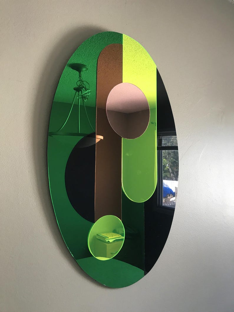 May include: A green, brown, and yellow oval mirror with a black background. The mirror is divided into sections with different colored shapes. The mirror is hanging on a wall.