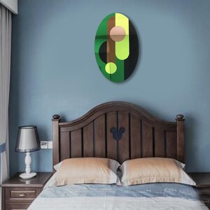 May include: A green, brown, black, and yellow abstract oval wall art piece with a geometric design. The art piece is hanging on a light blue wall above a wooden bed frame.