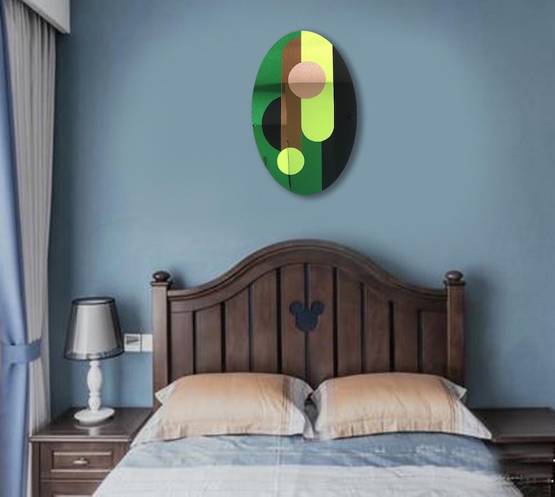 May include: A green, brown, black, and yellow abstract oval wall art piece with a geometric design. The art piece is hanging on a light blue wall above a wooden bed frame.