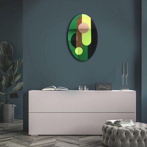 May include: A green, yellow, brown, and black abstract oval wall art piece with geometric shapes. The art piece is hanging on a dark blue wall above a white dresser.