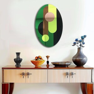 May include: A green, black, brown, and pink abstract oval wall art piece with geometric shapes. The art piece is hanging on a white wall above a wooden console table.