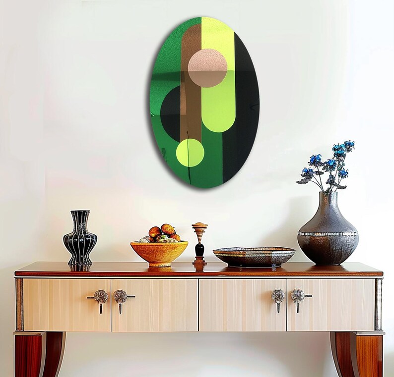 May include: A green, black, brown, and pink abstract oval wall art piece with geometric shapes. The art piece is hanging on a white wall above a wooden console table.
