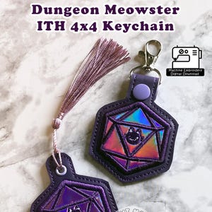 May include: Purple and iridescent keychain with a cat design. The keychain is shaped like a D20 die and has the text "Dungeon Meowster ITH 4x4 Keychain". Includes a tassel and a metal clasp. The design is by Mochi Makes Embroidery.