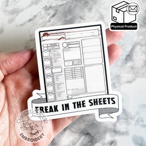 May include: A white sticker featuring a Dungeons & Dragons character sheet design with the text "FREAK IN THE SHEETS" on a banner. The sticker has a black border and is held in a hand.