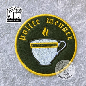 Può includere: Un cerotto rotondo di colore verde ricamato con un bordo giallo. Il cerotto presenta una tazza da tè bianca con un bordo dorato e vapore che ne esce. Il testo "polite menace" è ricamato in giallo intorno alla tazza da tè.
