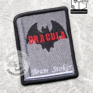 Può includere: Toppa ricamata con un design a pipistrello e la parola "DRACULA" in rosso. La toppa ha uno sfondo grigio con il testo "Bram Stoker" in bianco. La toppa è rettangolare con un bordo nero.