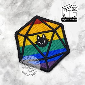 Può includere: Toppa ricamata a forma di dado D20, con una combinazione di colori arcobaleno e una faccia di gatto nero. La toppa ha un bordo nero. Il testo "MOCHI MAKES EMBROIDERY" e un'etichetta "Physical Product" sono visibili. Adatta per abbigliamento.