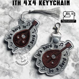 May include: Two keyrings with a mandolin design and the text "It's hard to be a bard." One keyring has a silver tassel. The text "HARD TO BE A BARD ITH 4X4 KEYYCHAIN" is at the top.