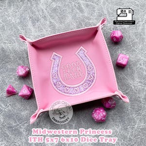 May include: Pink felt dice tray with a horseshoe design that says "Good Luck Babe" in pink thread. The tray is 13x18 cm and 15x25 cm.