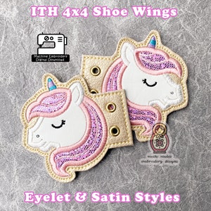 Puede incluir: Dos alas de zapatos de unicornio rosa y blanco con ojales dorados. Las alas miden 10,16 cm x 10,16 cm y están diseñadas para bordado a máquina. El texto "ITH 4x4 Shoe Wings" y "Eyelet & Satin Styles" es visible en la imagen.