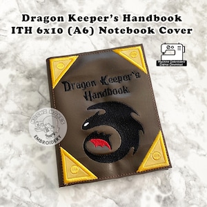 Puede incluir: Una cubierta de cuaderno marrón con el texto "Dragon Keeper's Handbook" y un diseño de dragón negro. La cubierta tiene detalles dorados en las esquinas y mide 15x25 cm. Es una descarga digital de bordado a máquina.