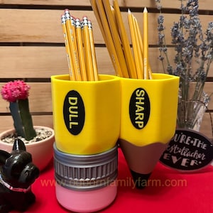 May include: A yellow pencil holder with two compartments, one labeled "DULL" and the other labeled "SHARP". The holder is filled with yellow pencils. The holder is sitting on a red surface.