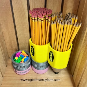 May include: A yellow pencil-shaped desk organizer with the word "DULL" and "SHARP" on the sides, filled with yellow pencils. A small container with the word "Erasers" on the side is filled with colorful erasers. The website address is at the bottom.