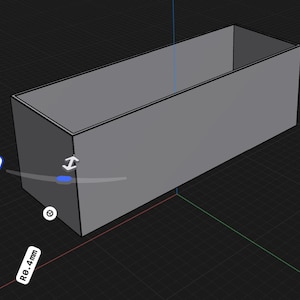 May include: A gray rectangular 3D model box with sharp edges, displayed in a digital design interface. The object features a visible corner radius measurement of R0.4mm, indicated by a white label and a blue interactive control point.