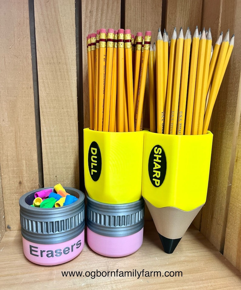 May include: A set of pencil-shaped desk organizers. The yellow pencil-shaped containers hold pencils labeled "DULL" and "SHARP". A smaller pink container labeled "Erasers" holds colorful erasers. The website address is visible at the bottom.