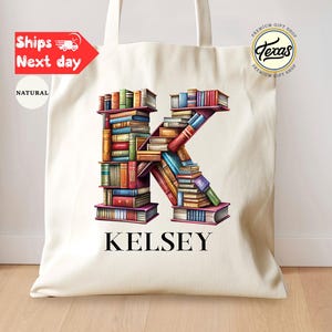 May include: A natural canvas tote bag featuring a colorful illustration of the letter "K" formed by stacked books. The name "Kelsey" is printed below the letter. The bag has two handles and a simple design.