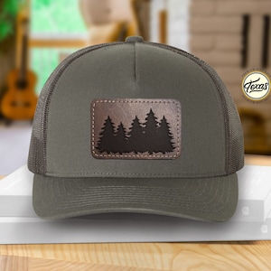 May include: A green and black trucker hat with a brown leather patch featuring a silhouette of a group of pine trees. The patch has the text "Texas" in a circle.
