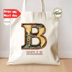 May include: Cream-colored tote bag featuring a large, decorative letter "B" with a vintage map design. The word "BELLA" is printed below the letter. The bag has long handles and a "Texas" logo.