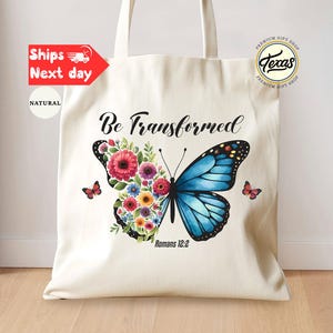 May include: Cream-colored tote bag featuring a butterfly design. One side of the butterfly is composed of colorful flowers, the other is blue. The text "Be Transformed" and "Romans 12:2" are printed on the bag. The bag has two handles.