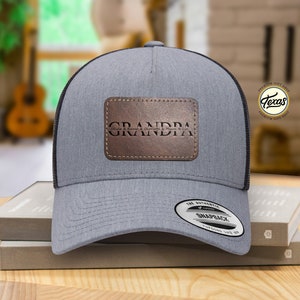 May include: A gray and black trucker hat with a brown leather patch that says "GRANDPA".