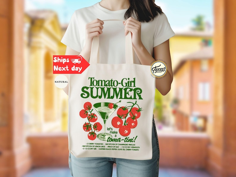 Peut inclure: Un sac fourre-tout en toile naturelle avec le texte "Tomato-Girl SUMMER" en vert. Le design comprend un verre &agrave; martini avec des tomates cerises et la phrase "let's make a toma-tini !" Les d&eacute;tails de la recette sont imprim&eacute;s en dessous.