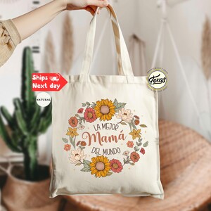 May include: A white canvas tote bag with a floral design and the text "La Mejor Mam&aacute; Del Mundo".