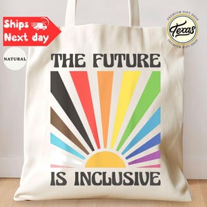 May include: Cream-colored tote bag with the text "THE FUTURE IS INCLUSIVE" in black. The design features a colorful sunburst with rainbow-colored rays. The bag has two handles and a "Texas Premium Gift Shop" logo.