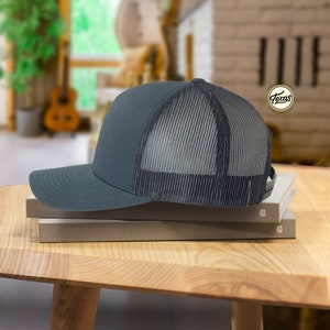 May include: A dark gray trucker hat with a black mesh back. The hat is sitting on top of two books.