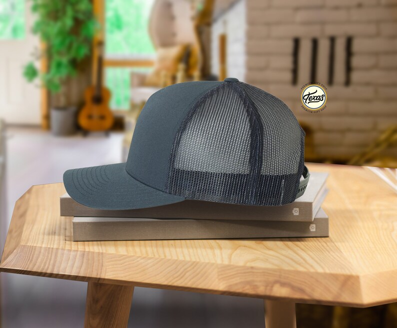 May include: A dark gray trucker hat with a black mesh back. The hat is sitting on top of two books.