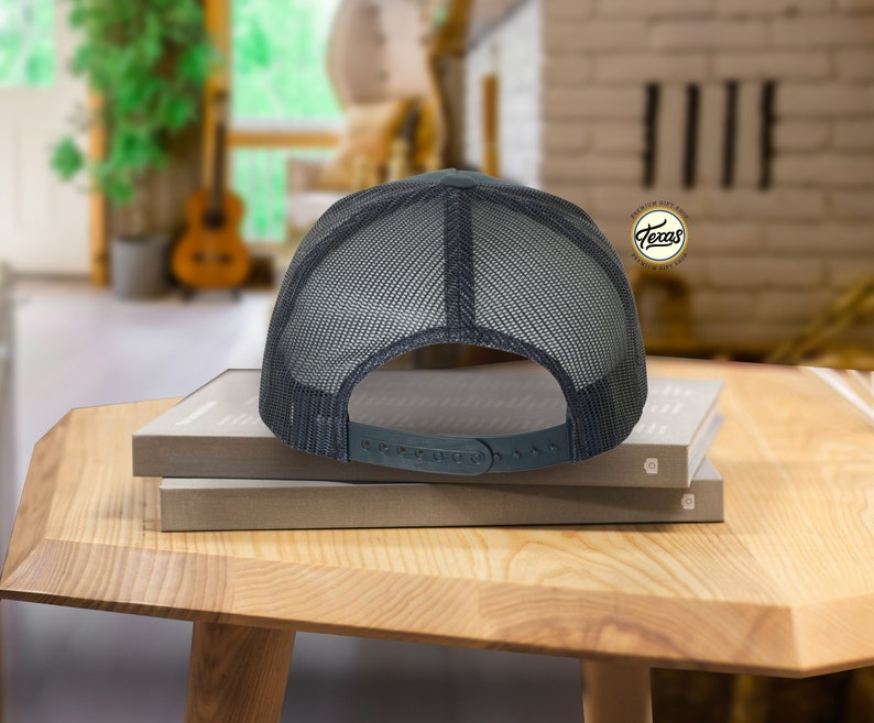 May include: A black and gray mesh trucker hat with a black adjustable strap. The hat is sitting on top of two books.