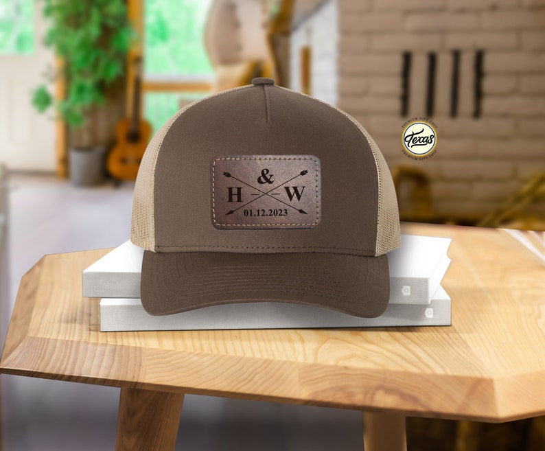 May include: Brown and tan trucker hat with a brown leather patch that says "H & W" with arrows and the date "01.12.2023".