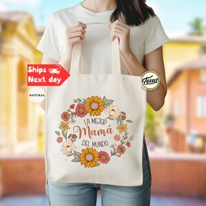 May include: A white tote bag with a floral design and the text "La Mejor Mam&aacute; Del Mundo".