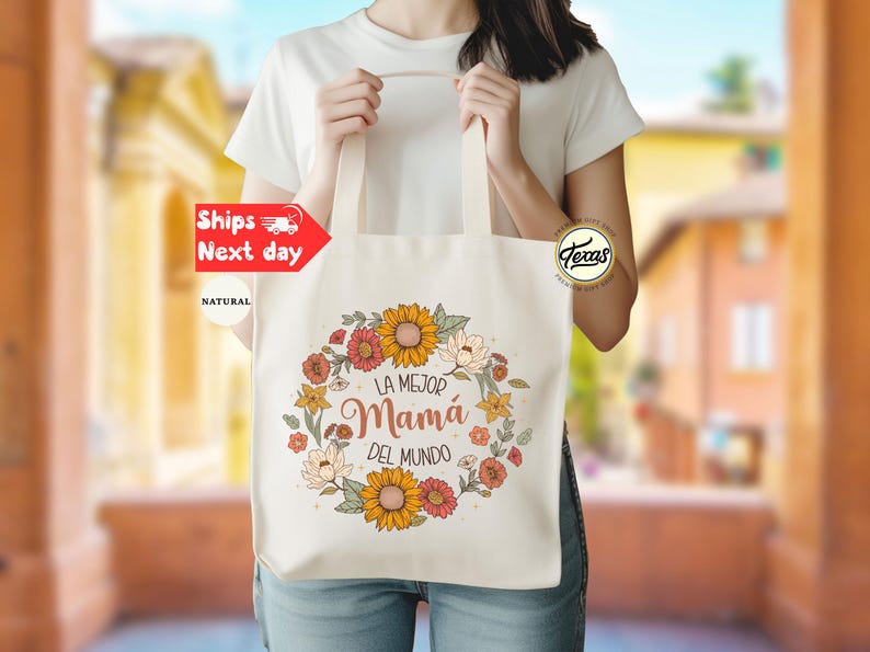 May include: A white tote bag with a floral design and the text "La Mejor Mam&aacute; Del Mundo".