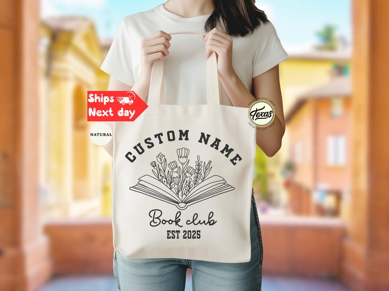 May include: Natural canvas tote bag with black text and a floral book design. The text reads "CUSTOM NAME" above an open book with flowers, and "Book club EST 2025" below. The bag has long handles.