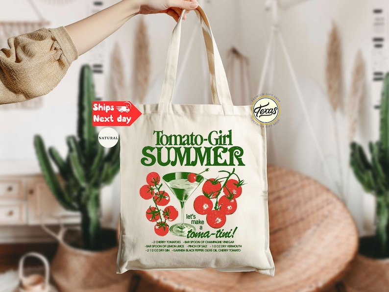 Peut inclure: Un sac fourre-tout en toile naturelle avec l'inscription "Tomato-Girl SUMMER" en vert, orn&eacute; d'une illustration de cocktail &agrave; la tomate. Le sac comprend &eacute;galement une recette de "toma-tini".