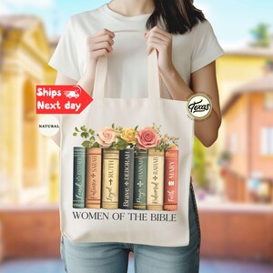 May include: A natural canvas tote bag featuring a floral design with pink and yellow roses above a row of illustrated books. The books are labeled with names like Esther, Sarah, and Ruth, with the text "WOMEN OF THE BIBLE" below.