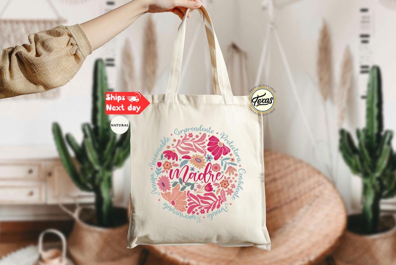 May include: A white canvas tote bag with a floral design and the word "madre" in the center. The design is surrounded by a circle of words in Spanish, including "comprendente", "protectora", "confiada", and "amable".