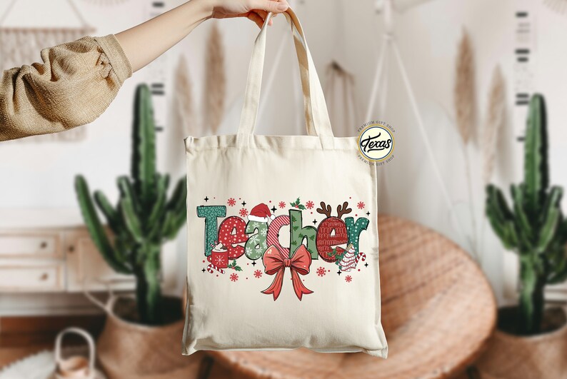 Puede incluir: Una bolsa de lona blanca con un dise&ntilde;o navide&ntilde;o que dice "Teacher" en letras de colores con un lazo rojo y copos de nieve.