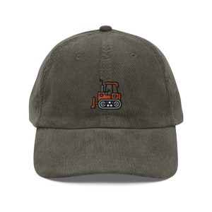 May include: A dark green corduroy baseball cap with an embroidered image of an orange bulldozer.