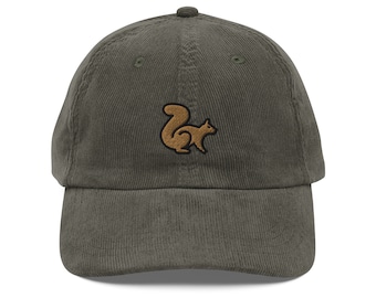 May include: Olive green corduroy baseball cap featuring a brown squirrel emblem. The cap has a curved brim and an adjustable strap. The squirrel design is embroidered on the front. This hat is a casual accessory.