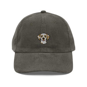 Op de afbeelding: Een groene corduroy baseball cap met een geborduurd honden gezicht. De hond is afgebeeld in wit, bruin en beige. De cap heeft een gebogen klep en een verstelbare band. Een modieus accessoire.