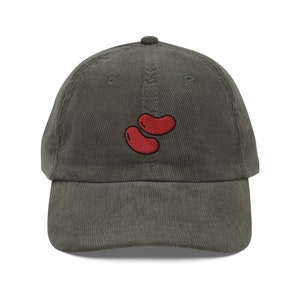 Peut inclure: Une casquette de baseball en velours côtelé vert foncé avec une image brodée rouge de deux haricots.