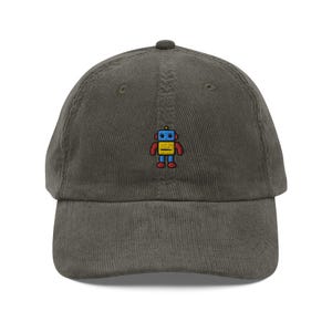 May include: A dark green corduroy baseball cap with an embroidered robot design. The robot is blue, yellow, and red.